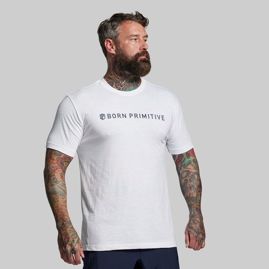 Man wearing a white 'Born Primitive' t-shirt against a gray background