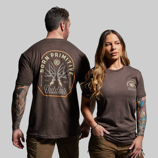Man and woman wearing brown t-shirts with 'Born Primitive' branding on a gray background