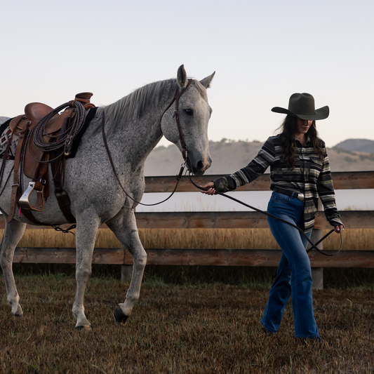Woman leading a gray horse by a wooden fence in an open field