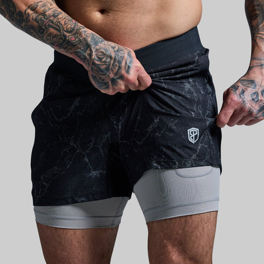 Person wearing black athletic shorts with a logo on a gray background