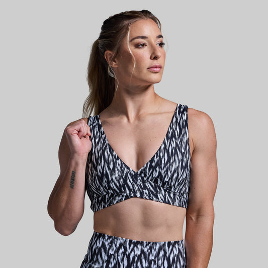 Woman wearing a black and white patterned sports bra and shorts on a plain background
