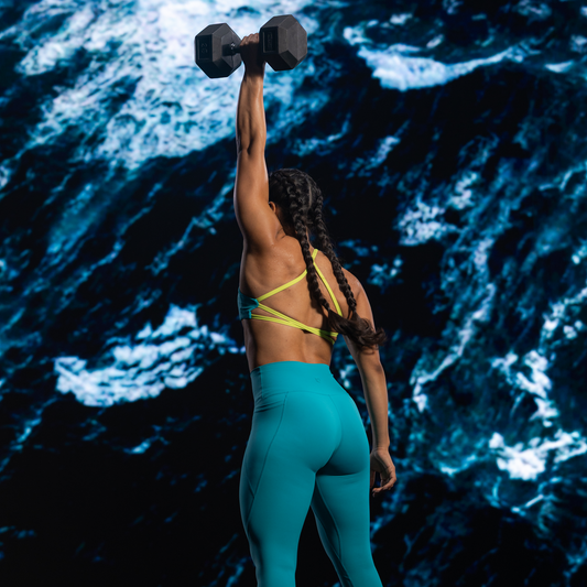 Person lifting a dumbbell in athletic wear with an ocean background