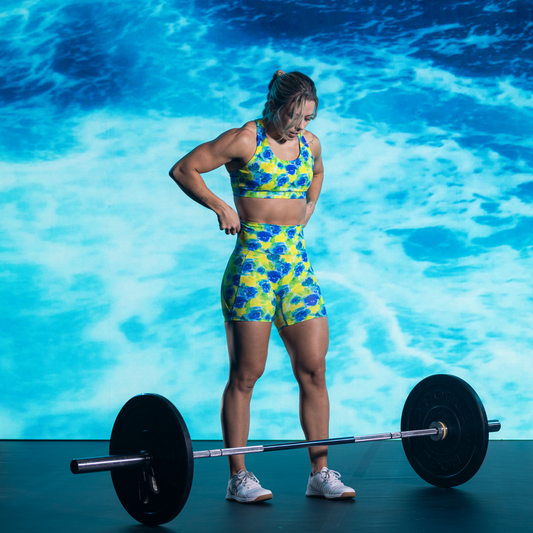 Woman in colorful athletic wear lifting a barbell against a blue water background