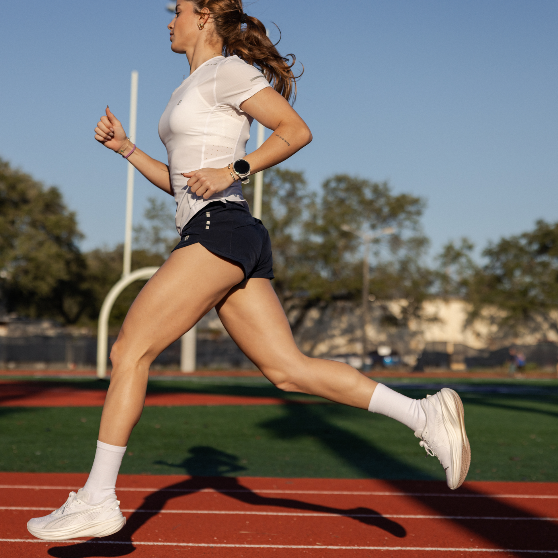 Women running on a track wearing navy running shorts, white running top and shoes.