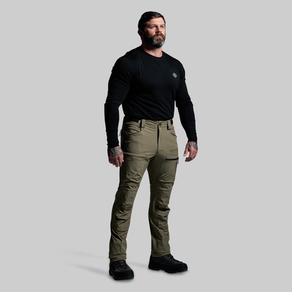 Man wearing a black long-sleeve shirt and green pants on a gray background