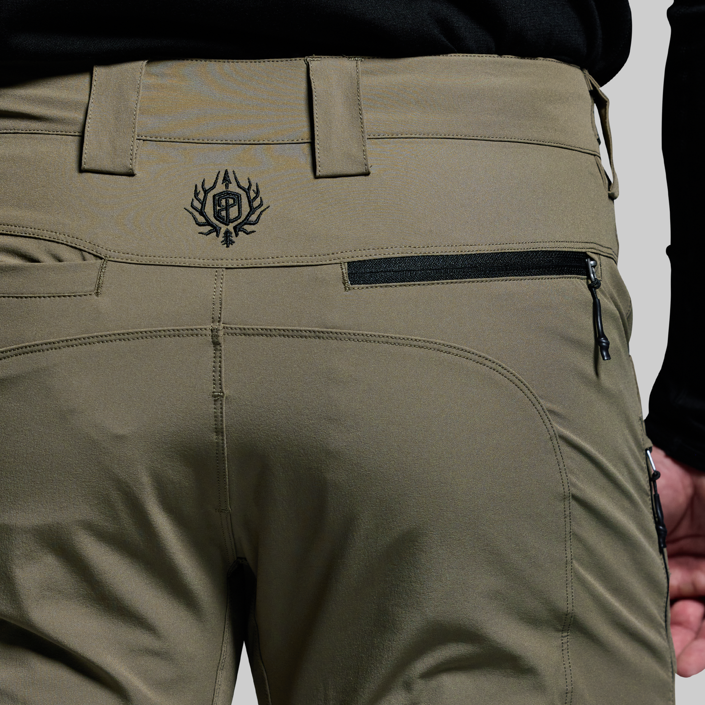 Close-up of olive green pants with a brand logo on a neutral background
