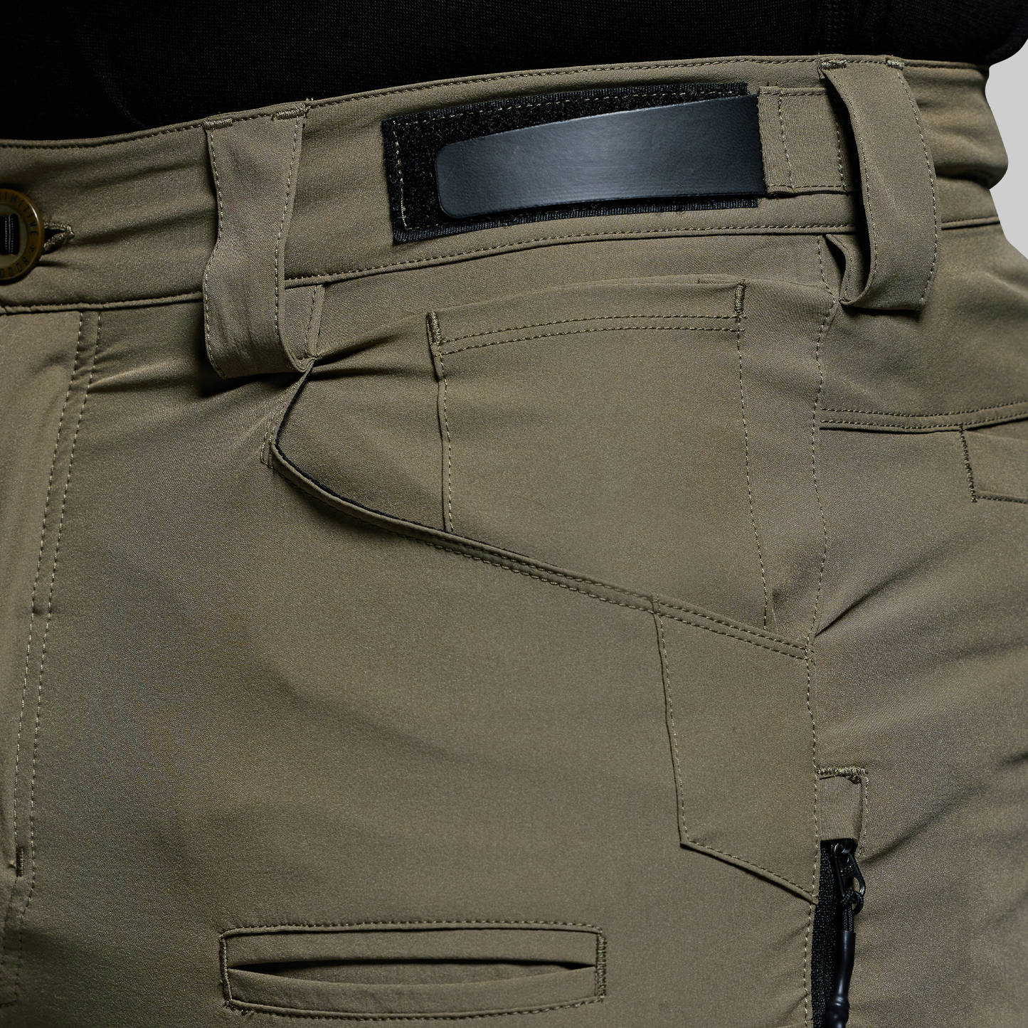 Close-up of olive green outdoor pants with a black adjustable waistband on a white background