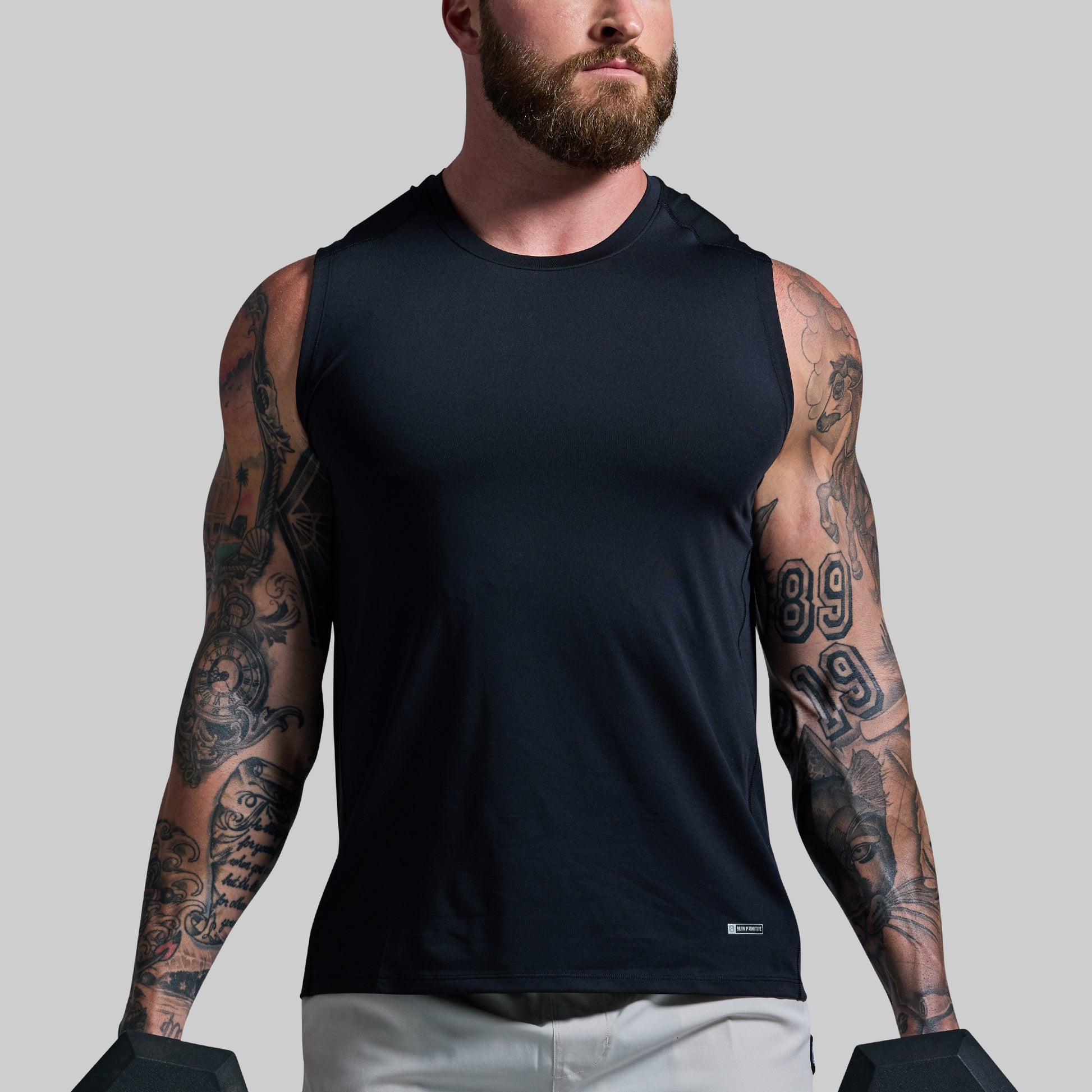 Man wearing a black sleeveless shirt with visible tattoos on arms against a gray background
