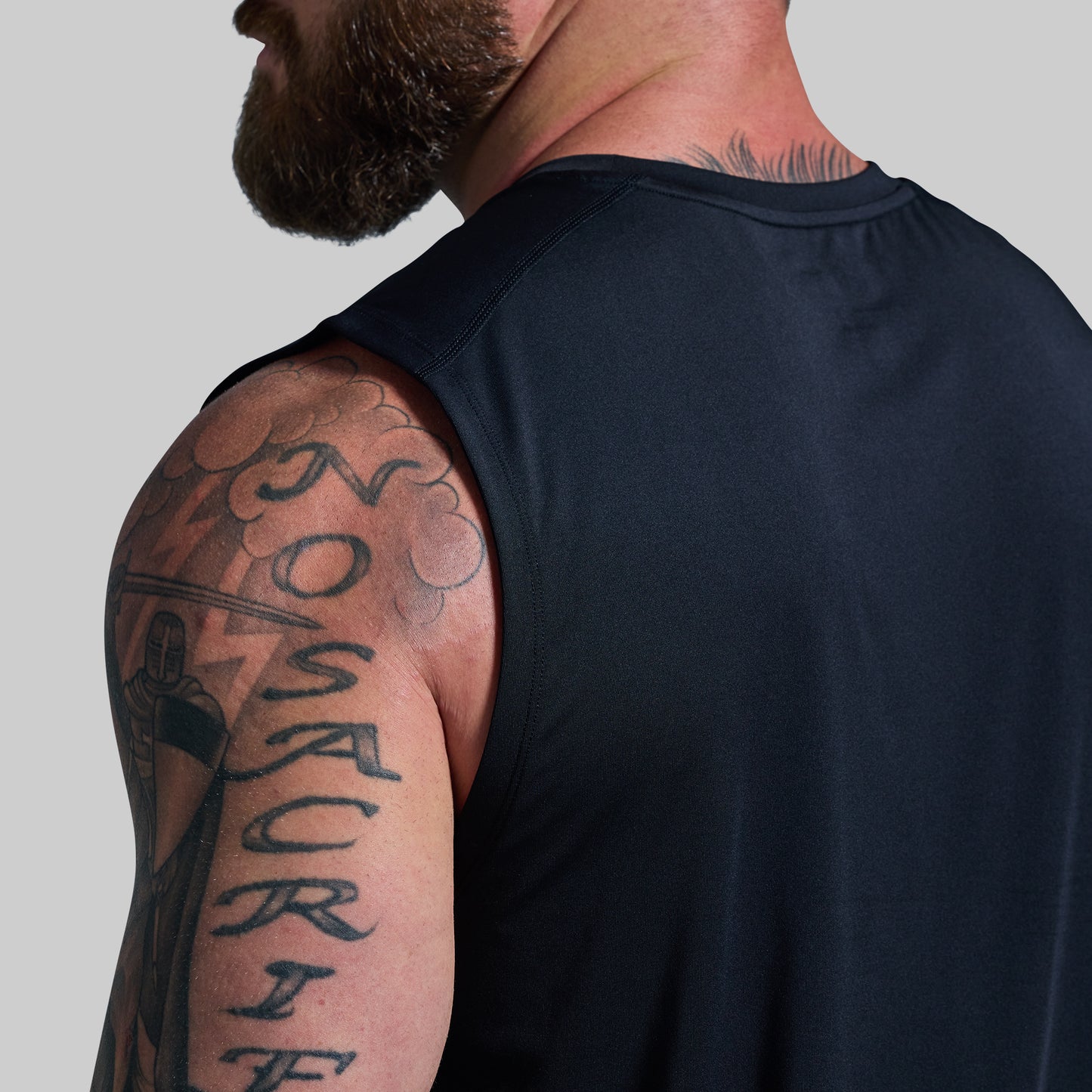 Man wearing a black sleeveless shirt with visible tattoos on his arm and shoulder.
