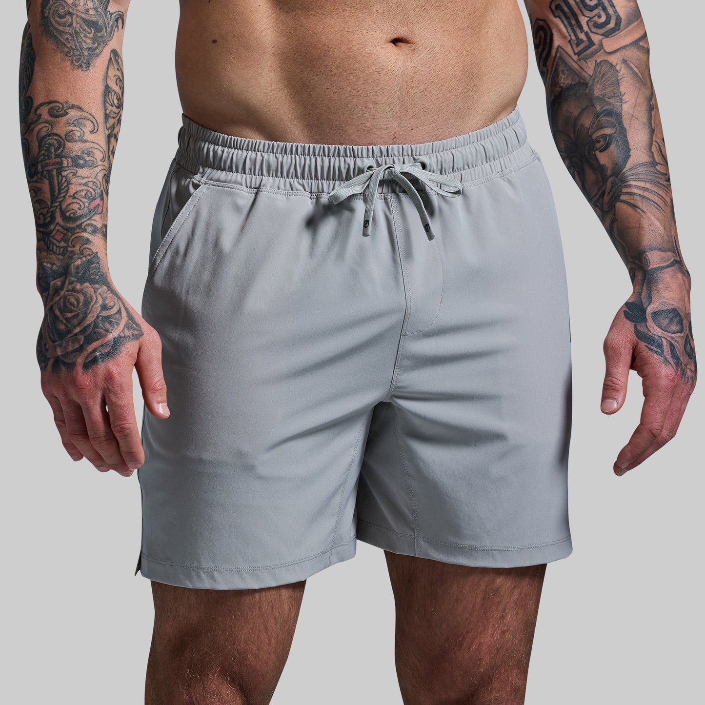 Person wearing gray shorts with tattooed arms on a plain background