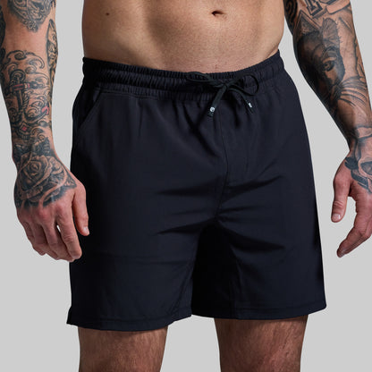 Person wearing black shorts with tattoos on arms against a gray background