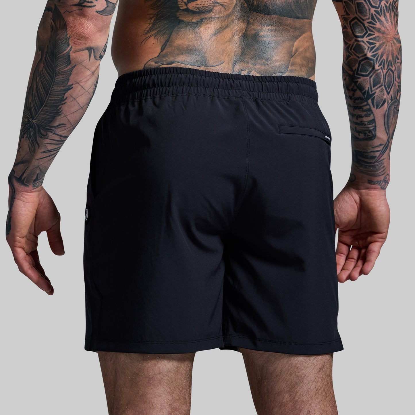Person wearing black shorts with tattoos on arms against a gray background