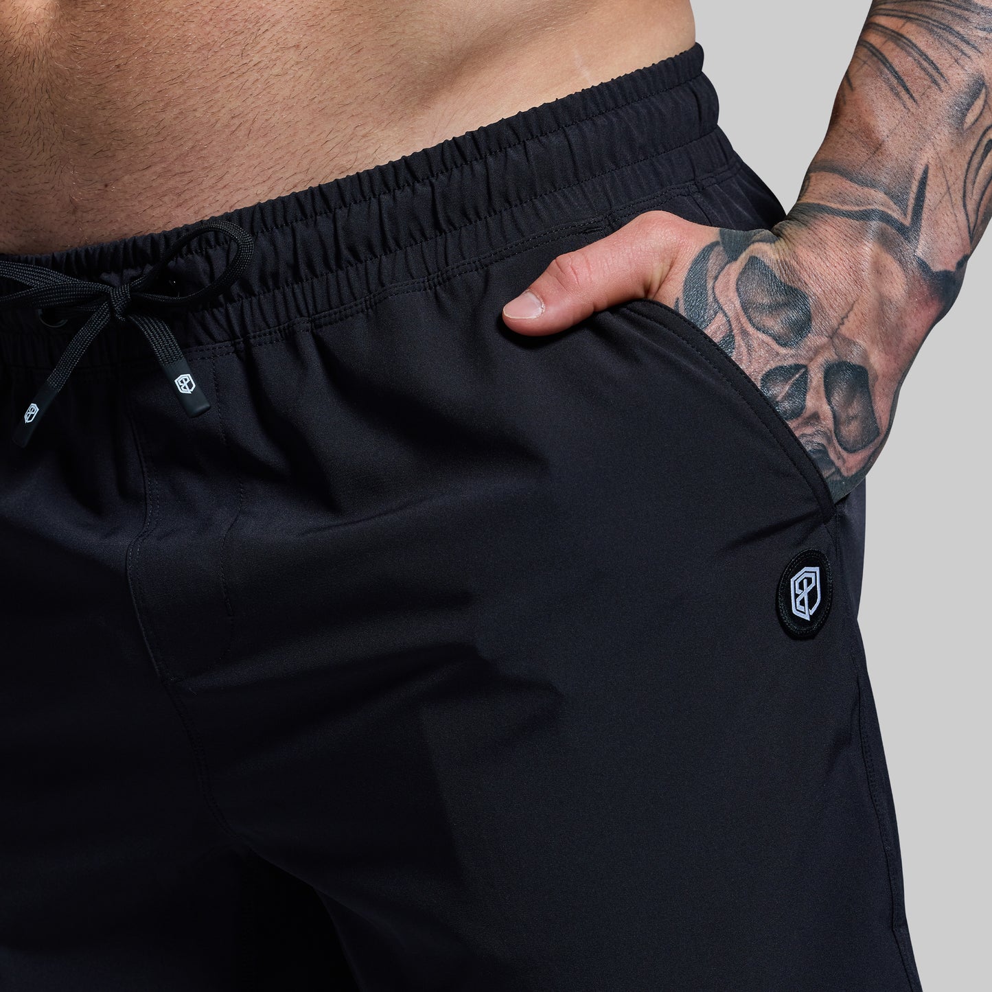 Person wearing black shorts with a visible brand logo on a plain background
