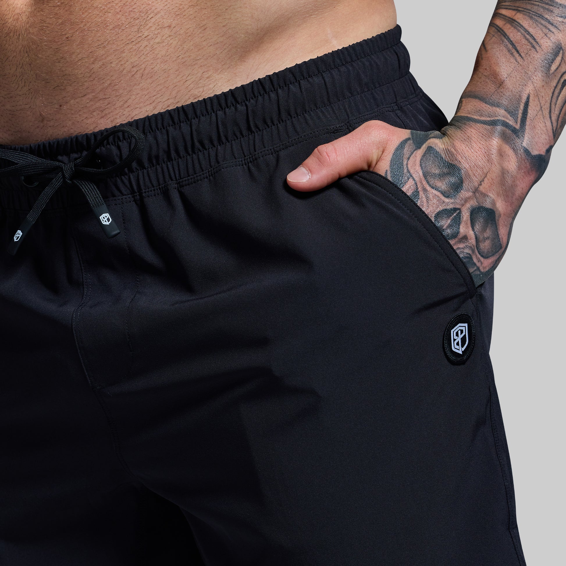 Person wearing black shorts with a visible brand logo on a plain background