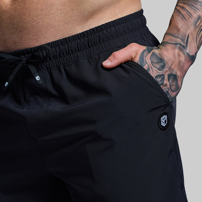 Person wearing black shorts with a visible brand logo on a plain background