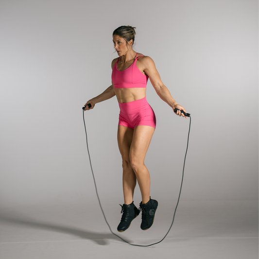 Woman in pink athletic wear jumping rope on a plain background
