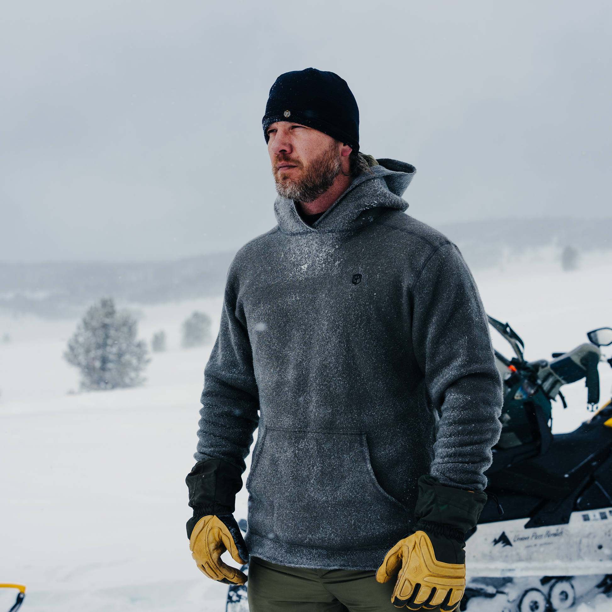 Man in winter clothing standing in a snowy landscape with a snowmobile.