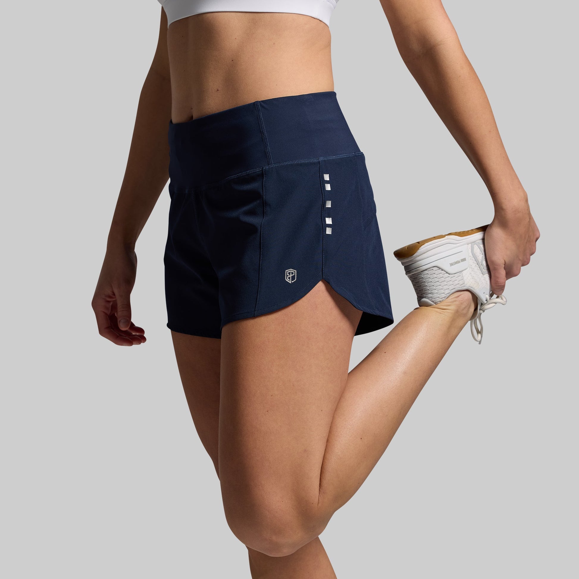 A pair of navy blue women's running shorts, shown from a side angle with a model stretching.