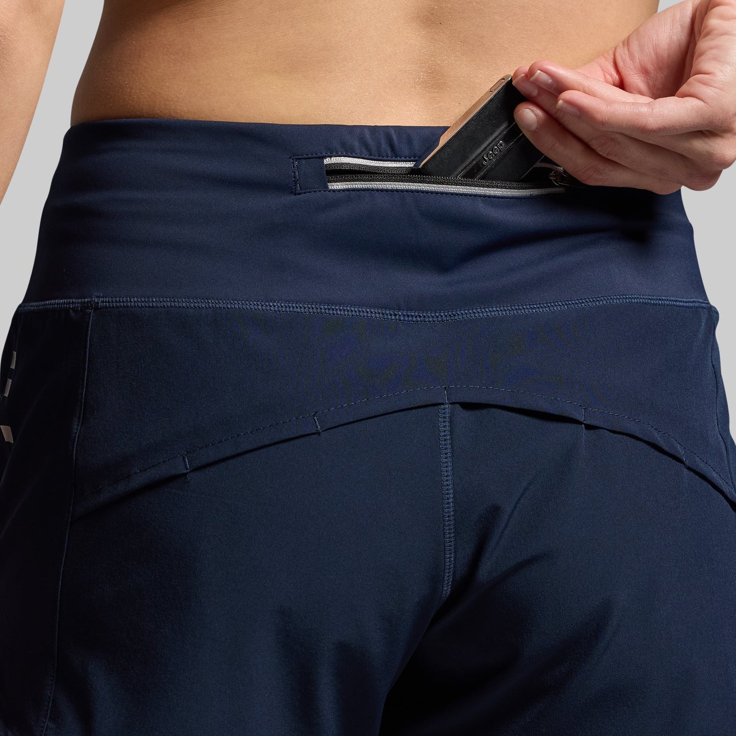 Person wearing navy blue shorts with a phone in the back pocket against a gray background
