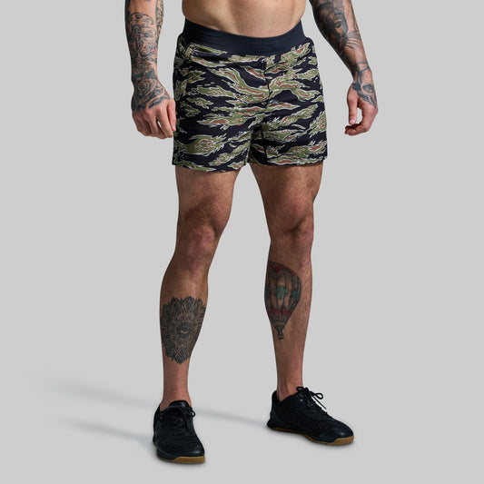 A person wearing a camouflage pattern athletic training shorts with built-in compression and pockets, standing against a plain background.