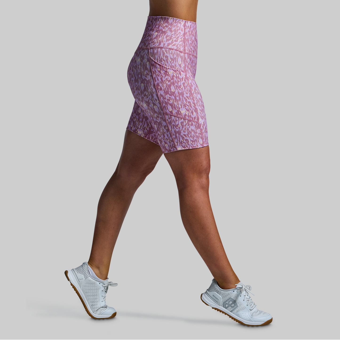 Person wearing a pink patterned athletic shorts and white sneakers on a gray background