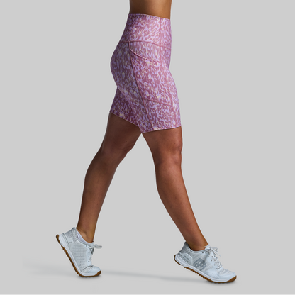 Person wearing a pink patterned athletic shorts and white sneakers on a gray background