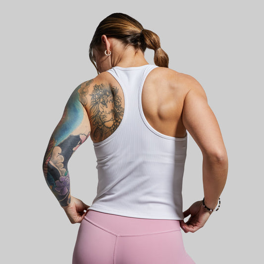 A woman wearing a white ribbed racerback tank top with a built-in bra, standing with her back towards the camera.