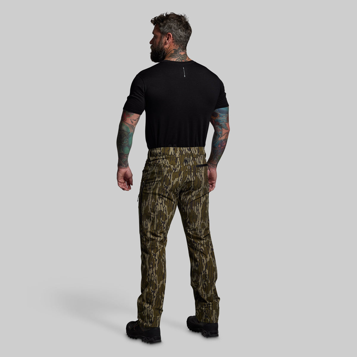 Man wearing camouflage pants and a black shirt on a gray background
