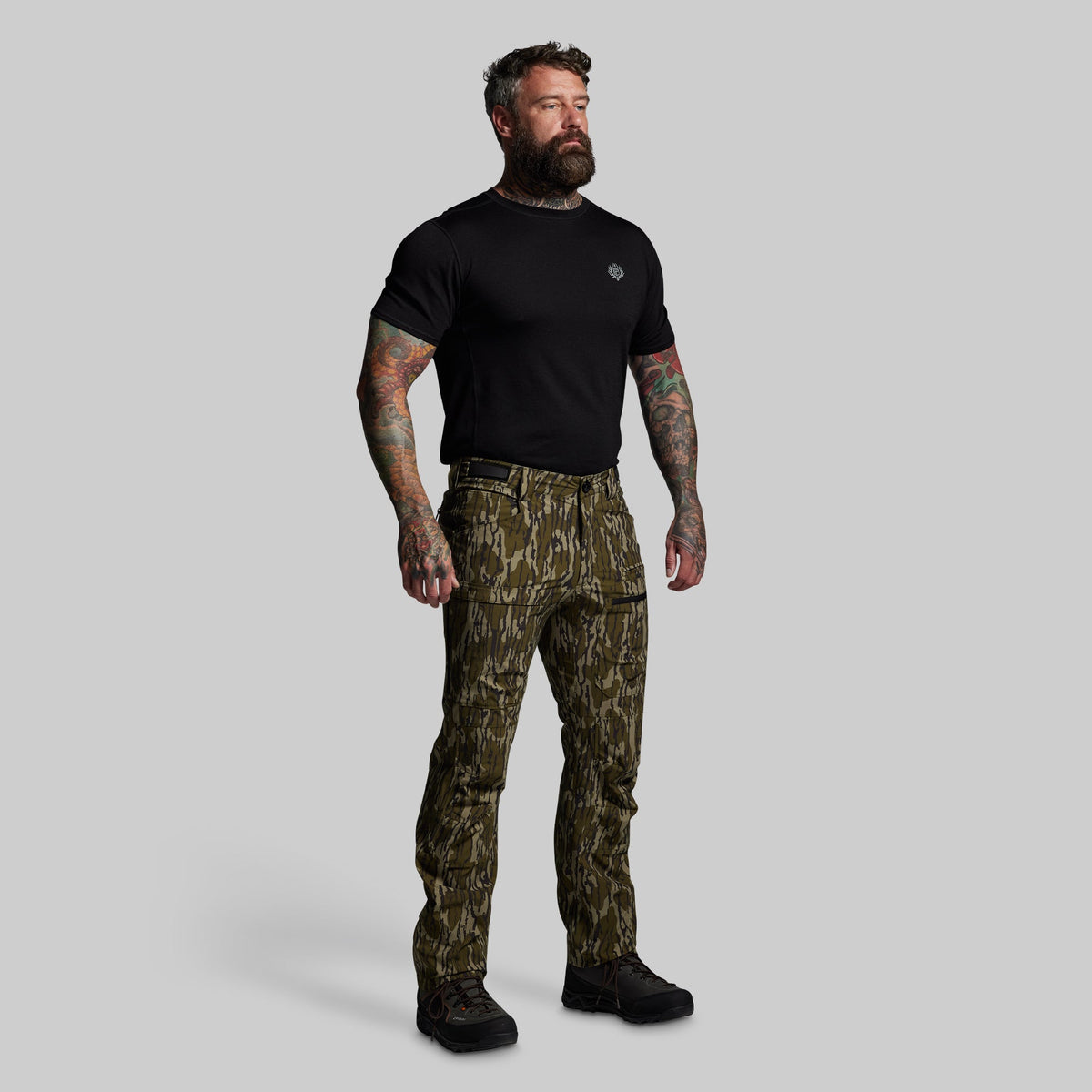 Man wearing camouflage pants and a black t-shirt on a gray background