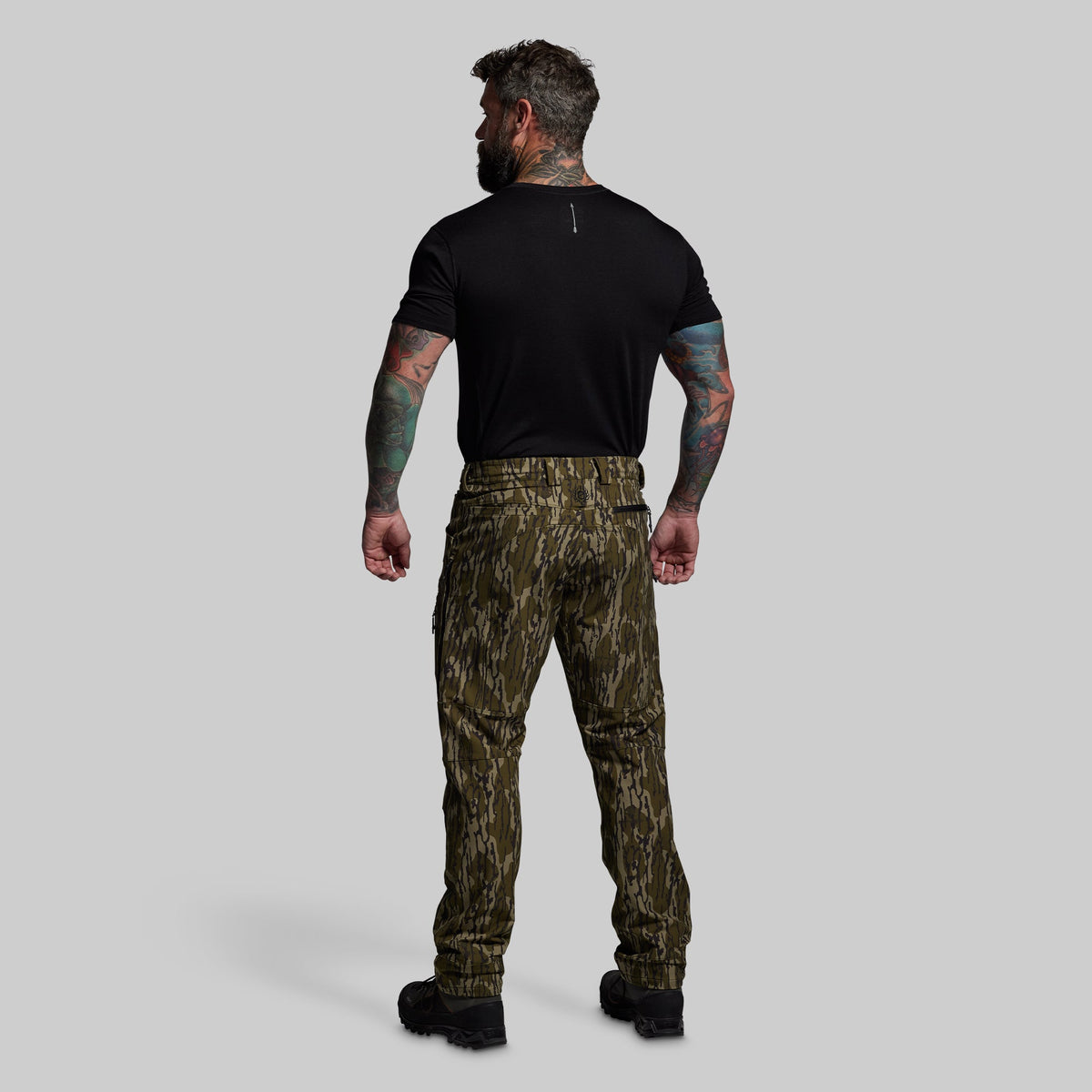 Man wearing camouflage pants and a black shirt on a gray background