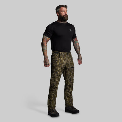 Man wearing a black t-shirt and camouflage pants on a gray background