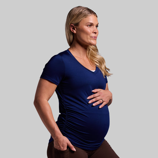 A pregnant woman wearing a short-sleeved blue V-neck shirt.