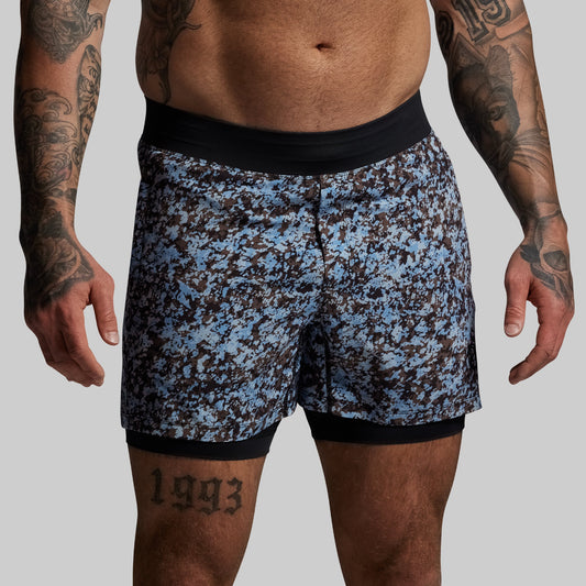 Blue and black patterned shorts worn by a person with tattoos on a gray background