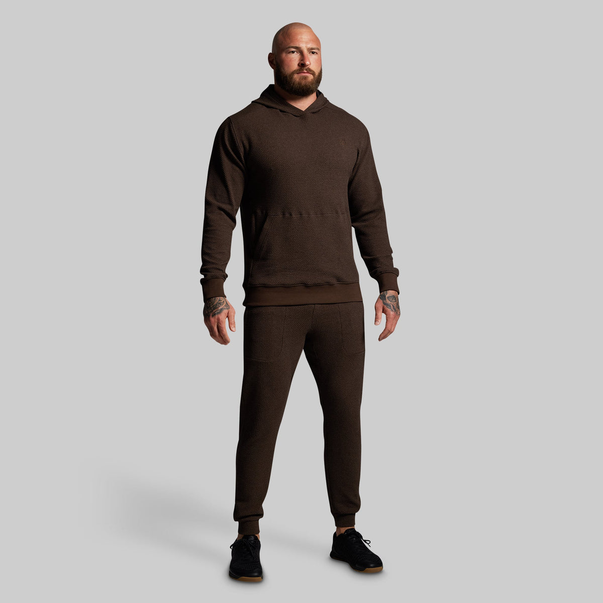 Man wearing a brown hoodie and pants on a gray background