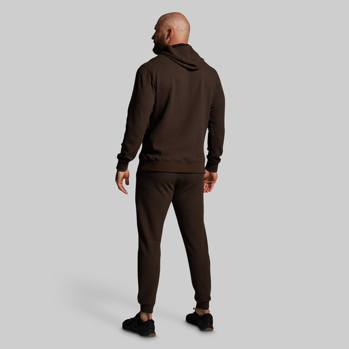 Man wearing a brown hoodie and joggers on a light gray background