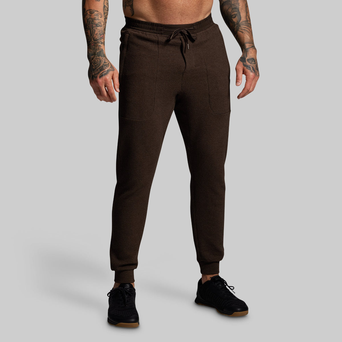 Brown jogger pants worn by a person on a gray background