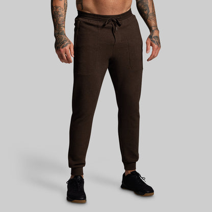 Brown jogger pants worn by a person on a gray background
