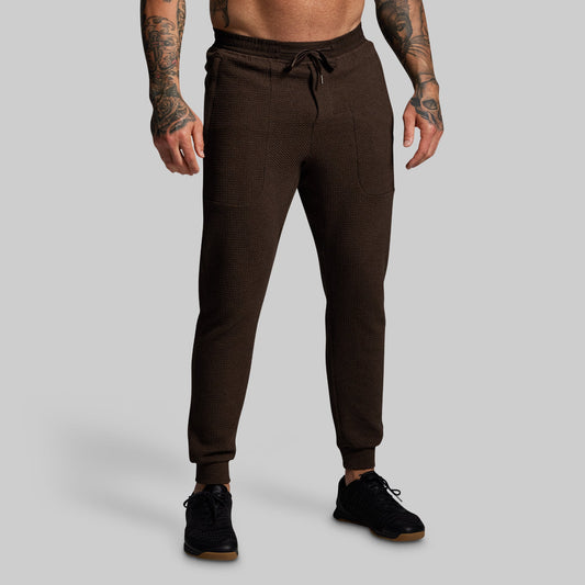 Brown jogger pants worn by a person on a gray background