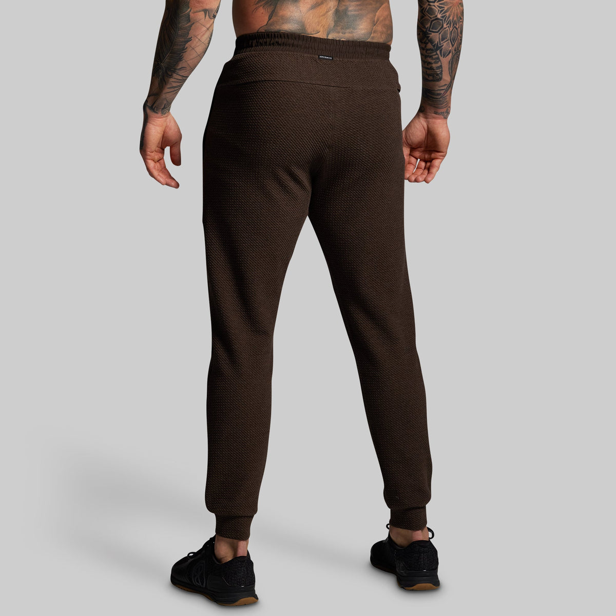 Brown jogger pants worn by a person on a gray background