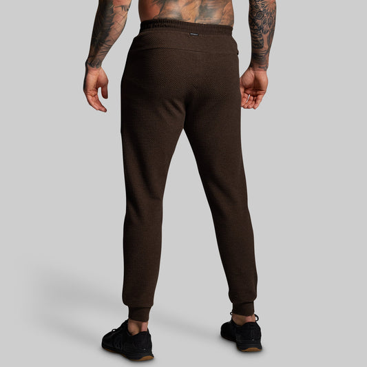 Brown jogger pants worn by a person on a gray background