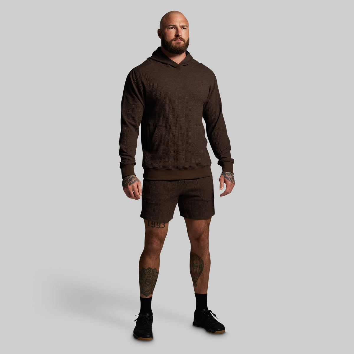 Man wearing a brown hoodie and shorts on a gray background