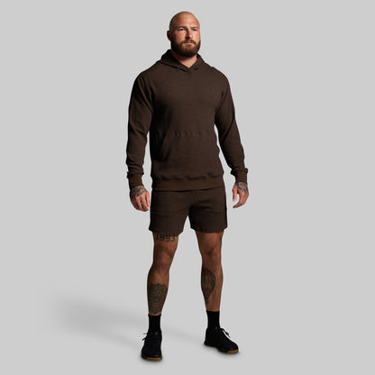 Man wearing a brown hoodie and shorts on a gray background
