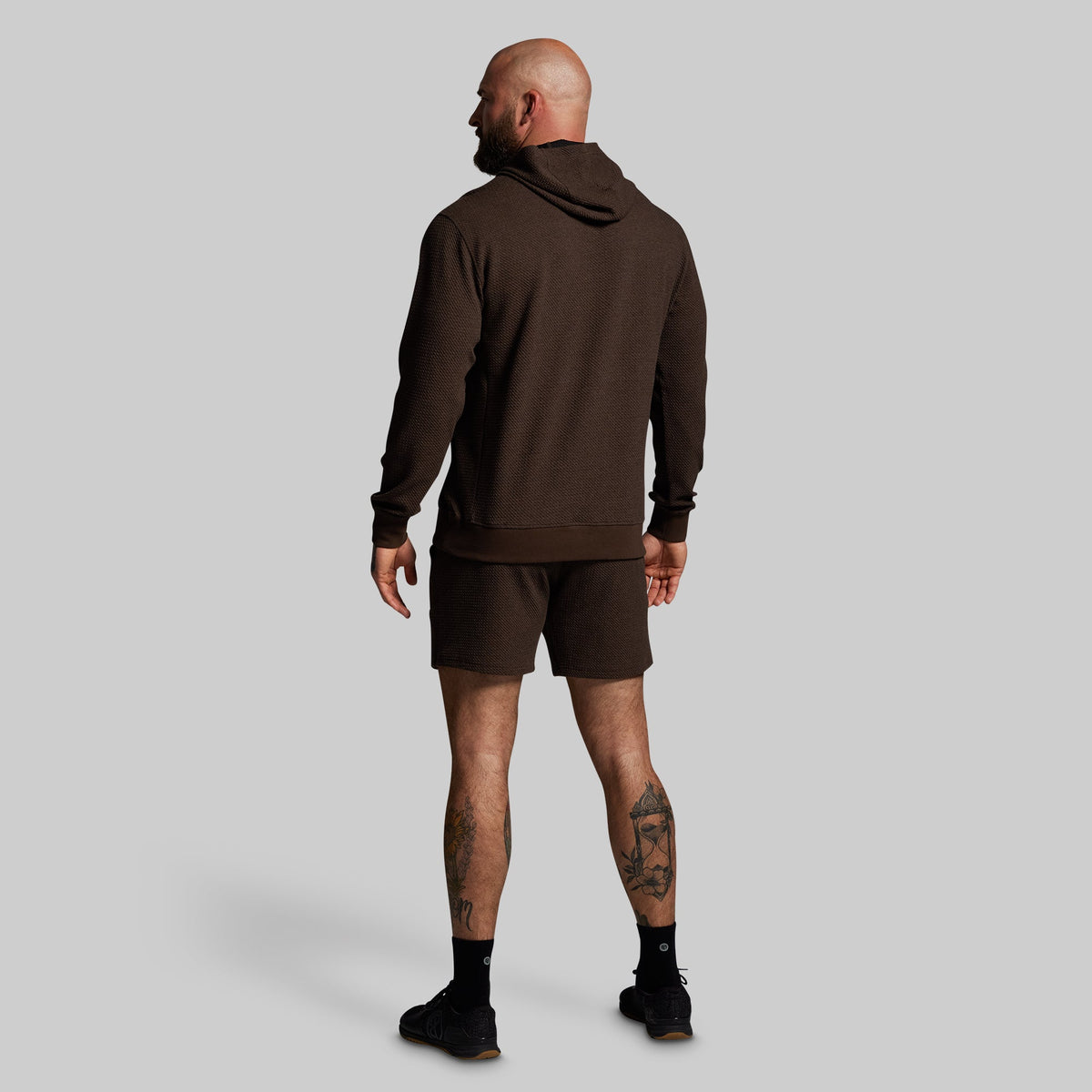 Man wearing a brown hoodie and shorts set on a gray background
