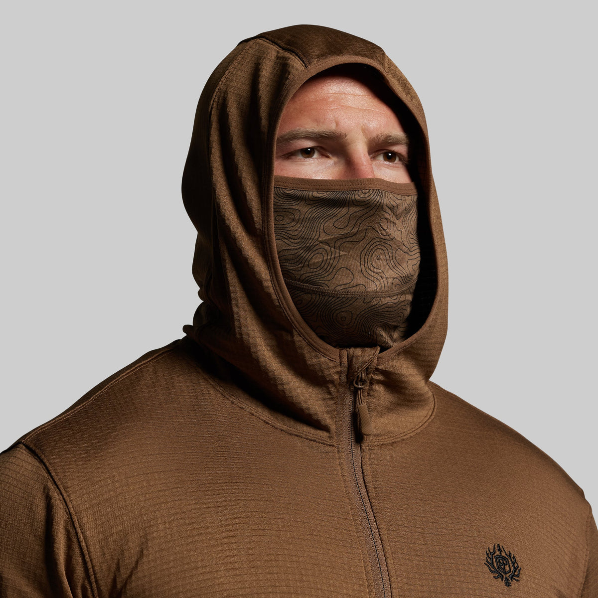 Person wearing a brown hoodie with a face mask on a gray background