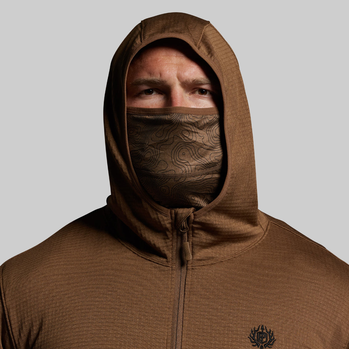 Person wearing a brown hoodie with a face covering on a gray background
