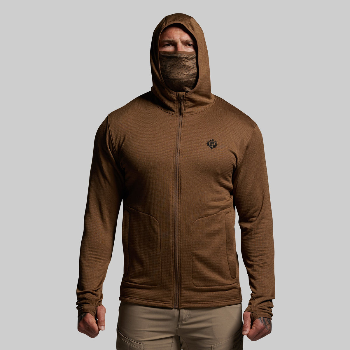Person wearing a brown hoodie with a face mask on a gray background