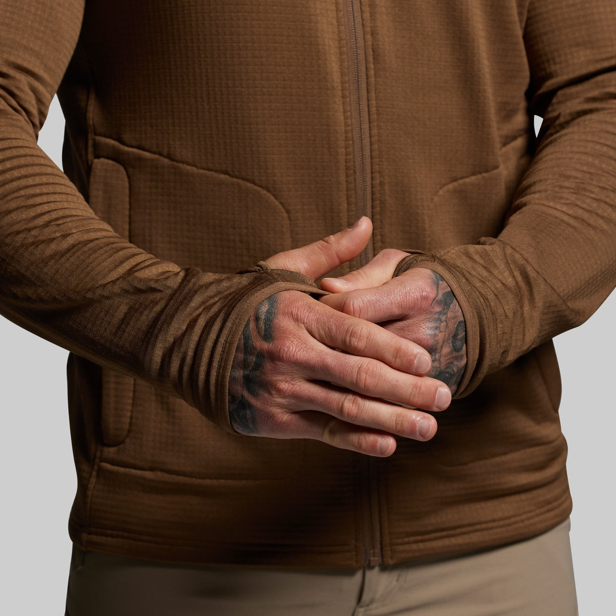 Person wearing a brown full zip hoodie with tattooed hands on a neutral background