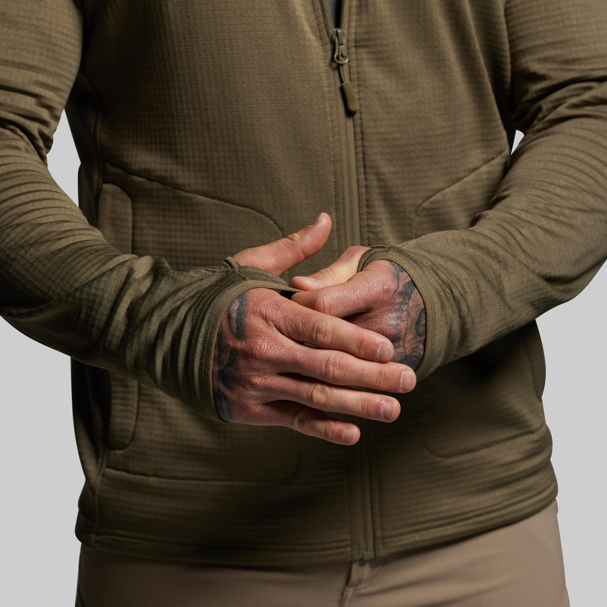 Person wearing a green hoodie with tattooed hands on a neutral background