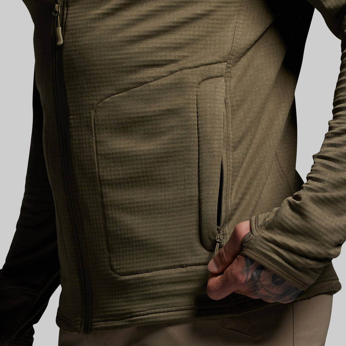 Close-up of a person wearing a green full zip hoodie with a pocket on a gray background