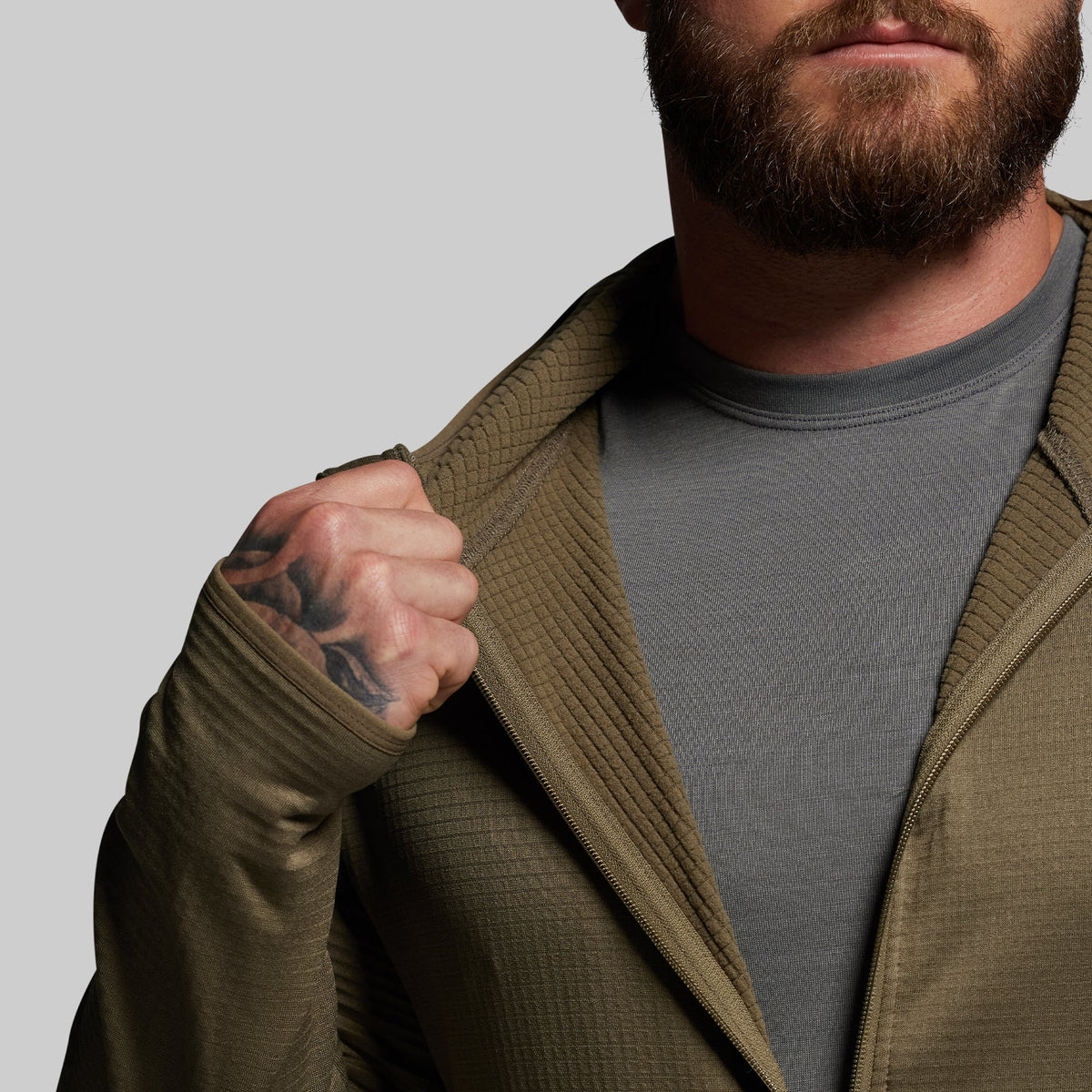 Man wearing a green zip up over a gray shirt against a plain background